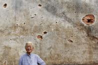 An elderly woman poses in front of a bullet-riddled wall of her house in the village of Guningtou in Kinmen, Taiwan, September 7, 2015. REUTERS/Pichi Chuang