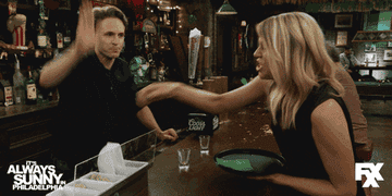 Two characters from "It's Always Sunny in Philadelphia" are engaged in a playful slap fight at a bar