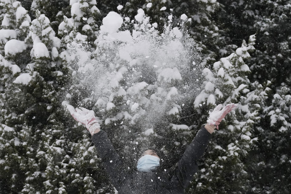 A woman wearing a mask throws snow in the air during a snow fall in Beijing, China, Sunday, Nov. 7, 2021. An early-season snowstorm has blanketed much of northern China including the capital Beijing, prompting road closures and flight cancellations. (AP Photo/Ng Han Guan)