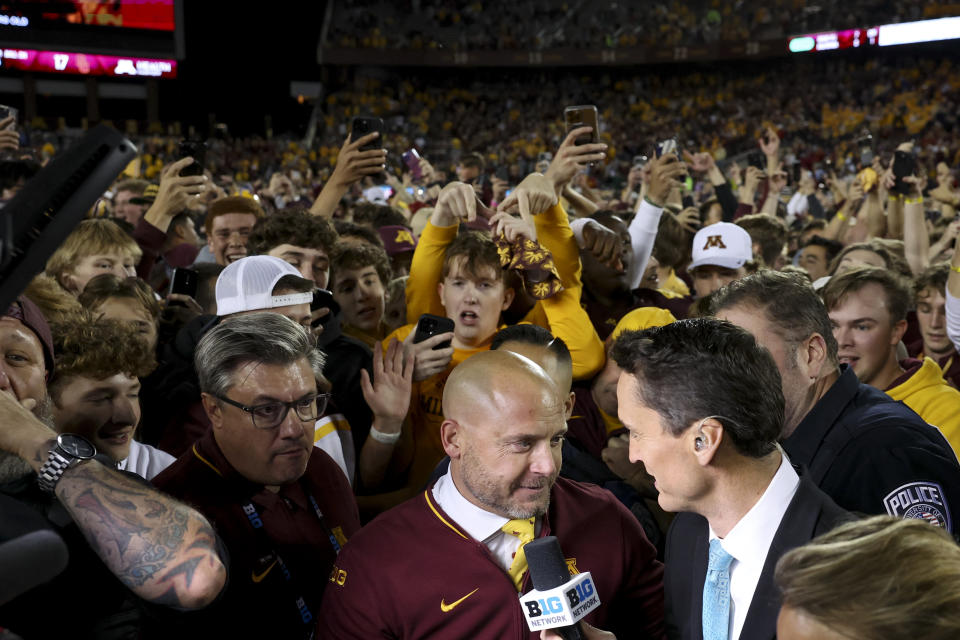 Minnesota head coach P.J. Fleck speaks to a reporter while fans swarm him on the field after his team won an NCAA college football game against Southern California Saturday, Oct. 5, 2024, in Minneapolis. (AP Photo/Ellen Schmidt)