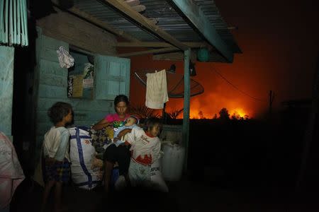 A mother gives a drink to her son as she prepares to leave her house with her children, after a forest fire spread close to their home near Dumai, as haze covers Indonesia's Riau province in this June 20, 2013 file photograph. REUTERS/Beawiharta/Files