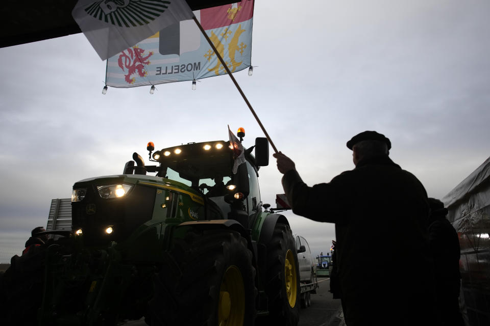 A farmer waves to a tractor at a barricade as farmers block a highway Tuesday, Jan. 30, 2024 in Jossigny, east of Paris. With protesting farmers camped out at barricades around Paris, France's government hoped to calm their anger with more concessions Tuesday to their complaints that growing and rearing food has become too difficult and not sufficiently lucrative. (AP Photo/Christophe Ena)