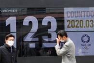 Passersby, wearing face masks due to the outbreak of the coronavirus disease (COVID-19), walk past a screen counting down the days to the Tokyo 2020 Olympic Games in Tokyo