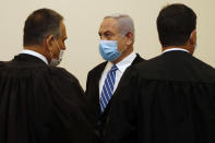 Israeli Prime Minister Benjamin Netanyahu, center, wearing a face mask in line with public health restrictions due to the coronavirus pandemic, stands with his lawyers inside the court room as his corruption trial opens at the Jerusalem District Court, Sunday, May 24, 2020. He is the country’s first sitting prime minister ever to go on trial, facing charges of fraud, breach of trust, and accepting bribes in a series of corruption cases stemming from ties to wealthy friends. (Ronen Zvulun/ Pool Photo via AP)