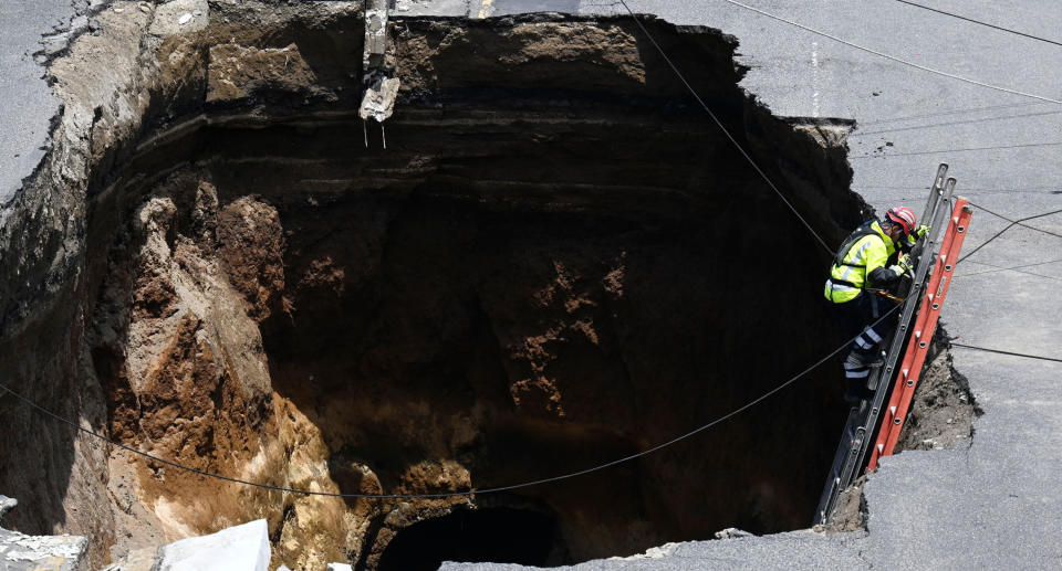 A rescuer walks down a staircase into a giant hole in a road, caused by the collapse of a drainage system due to heavy rains that hit Guatemala