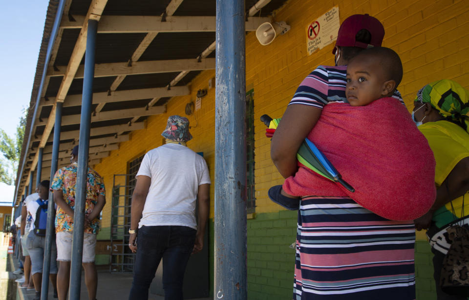 A woman with a child on her back joins a queue to cast her vote in local elections in Soweto, Monday, Nov. 1, 2021. South Africa is holding crucial local elections Monday, the country has been hit by a series of crippling power blackouts that many critics say highlight poor governance. (AP Photo/Denis Farrell)