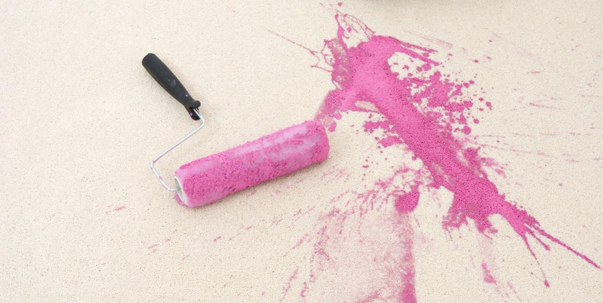 paint roller and tray with pink paint spilled on a cream rug