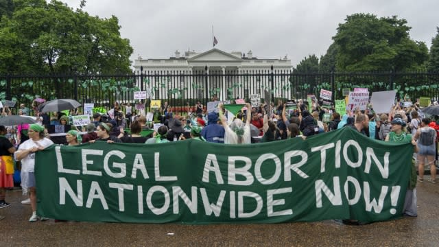 Abortion-rights protesters shout slogans and display banners after tying green flags to the fence of the White House.