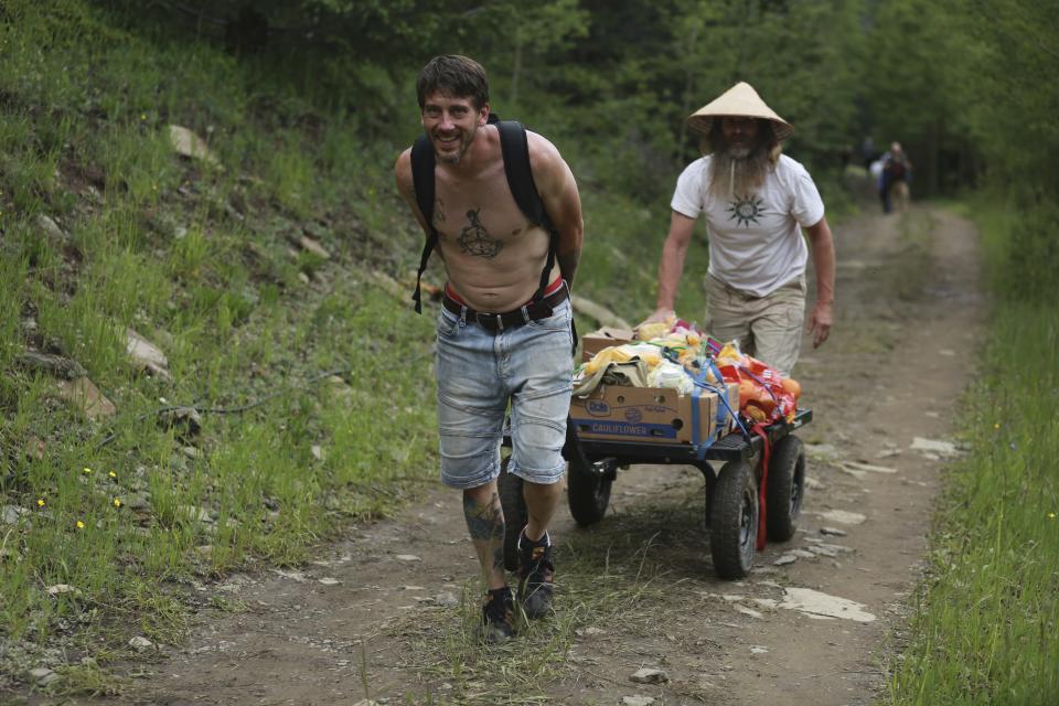 Rainbow Gathering participants carry food up a hill from the parking lot toward campsites on Friday, July 2, 2021, in the Carson National Forest, outside of Taos, N.M. More than 2,000 people have made the trek into the mountains of northern New Mexico as part of an annual counterculture gathering of the so-called Rainbow Family. While past congregations on national forest lands elsewhere have drawn as many as 20,000 people, this year’s festival appears to be more reserved. Members (AP Photo/Cedar Attanasio)