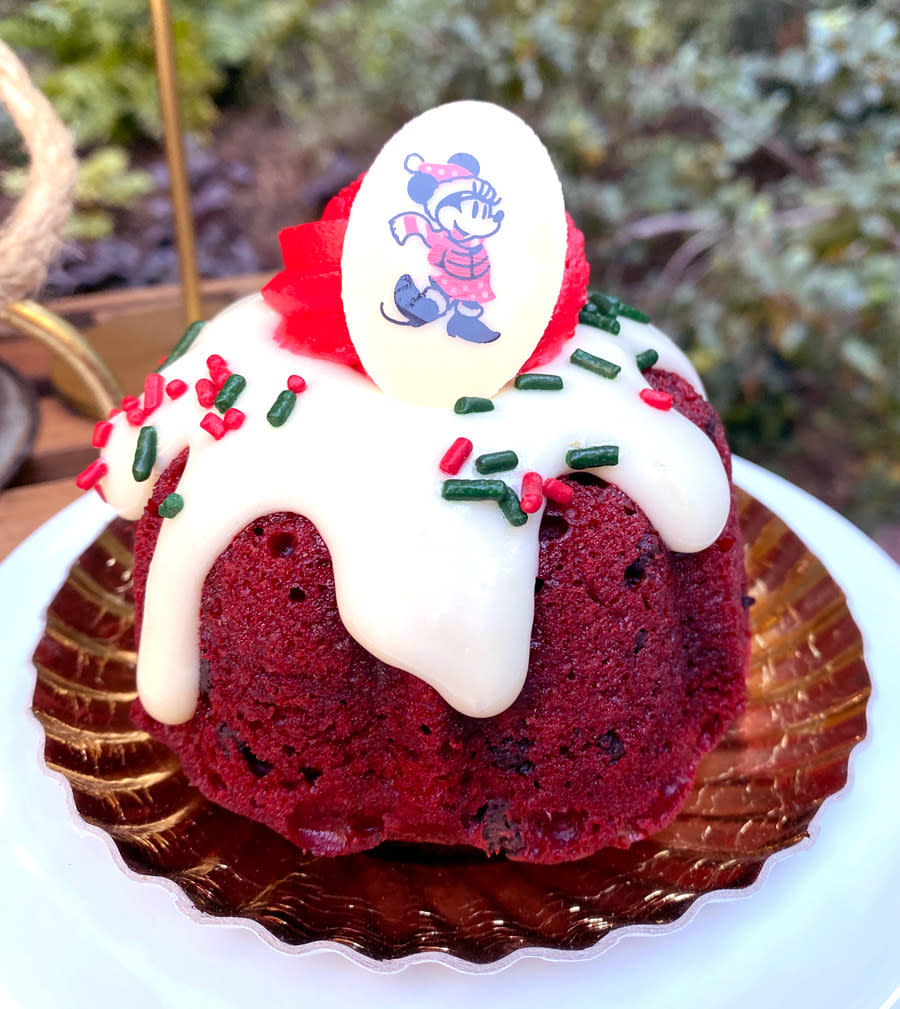 A small red velvet bundt cake topped with frosting, sprinkles, and a white chocolate piece that has minnie printed on it