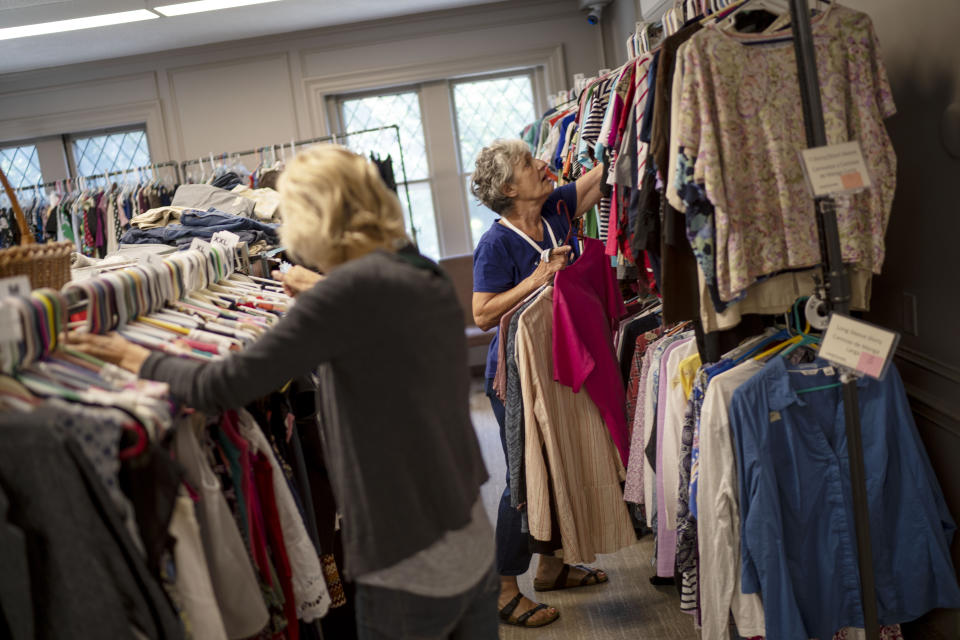 Volunteers Katherine Flynn, right, and Enid Schaefer stock donated clothes on a rack in the community outreach center at Asbury First United Methodist Church, Tuesday, Aug. 22, 2023, in Rochester, N.Y. Asbury is roughly 3 miles (5 kilometers) from much poorer neighborhoods north and west where most of the city's shootings take place. The congregation, though, is committed to taking on problems beyond its doorstep. It has expanded a home it owns next door into a community outreach center, providing clothing, showers, laundry and other help to people in need, while serving 35,000 meals a year. (AP Photo/David Goldman)