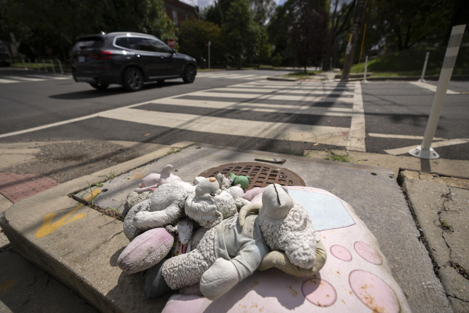 A vehicle drives past toys left at a memorial for 5-year-old Allie Hart, who was struck and killed in 2021 by a driver while riding her bicycle in a crosswalk, Monday, Sept. 11, 2023, in Washington. (AP Photo/Mark Schiefelbein)