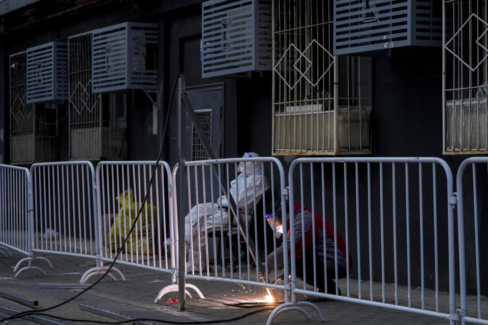 A worker in protective suit keeps watch as a worker welds on a steel frame to install metal barriers in a locked down neighborhood as part of COVID-19 controls in Beijing, Thursday, Nov. 24, 2022. China is expanding lockdowns, including in a central city where factory workers clashed this week with police, as its number of COVID-19 cases hit a daily record.(AP Photo/Andy Wong)