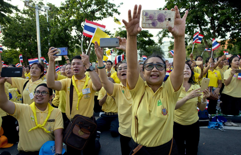 In this May 5, 2019, photo, people on their knees, reach up to take pictures of King Maha Vajiralongkorn as he passes through the streets during his coronation ceremony in Bangkok, Thailand. King Maha Vajiralongkorn was officially crowned amid the splendor of the country's Grand Palace, taking the central role in an elaborate centuries-old royal ceremony that was last held almost seven decades ago. (AP Photo/Gemunu Amarasinghe)