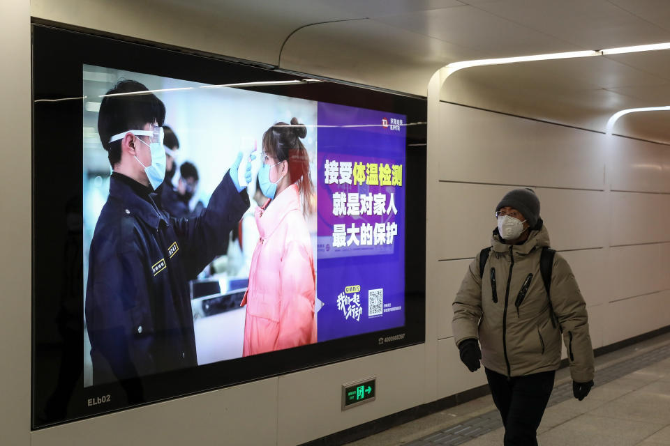 A person wears a protective face mask in Beijing while walking past a sign warning people to wear face masks due to coronavirus.