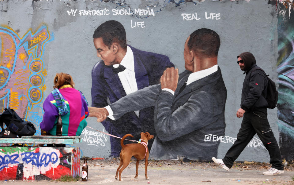 BERLIN, GERMANY - MARCH 30: Graffiti depicting a meme showing actor Will Smith slapping comedian Chris Rock, criticizes idealized self-portrayals of social media users&#39; lives, on a former section of the Berlin Wall on March 30, 2022 in Berlin, Germany. Will Smith slapped Chris Rock in the face on stage during the 94th Academy Awards ceremony, when the comic made a joke about the actor&#39;s wife, Jada Pinkett Smith, after which actor Smith picked up the first Oscar of his career for his role playing the father of tennis players Venus and Serena Williams in the film 