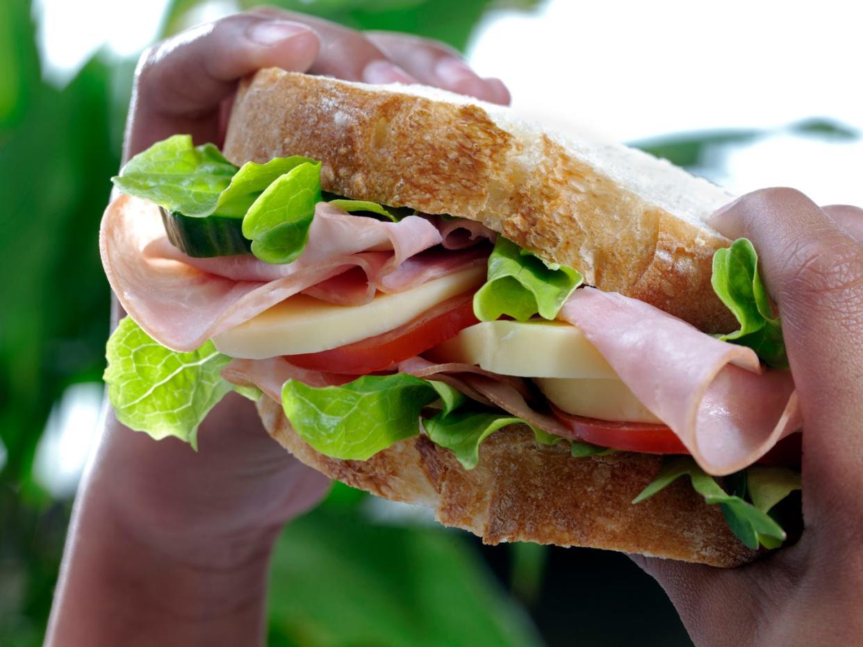 Close up of a large ham sandwich held in small black hands