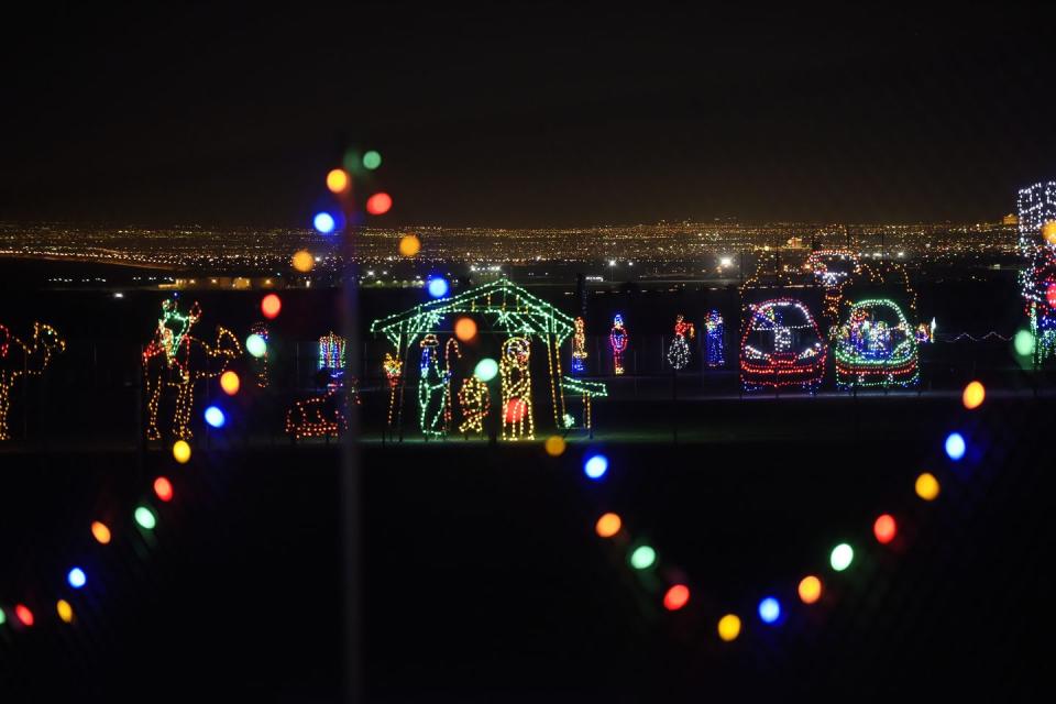 string of lights in foreground, with light displays in middle ground, in background are the white lights of the city