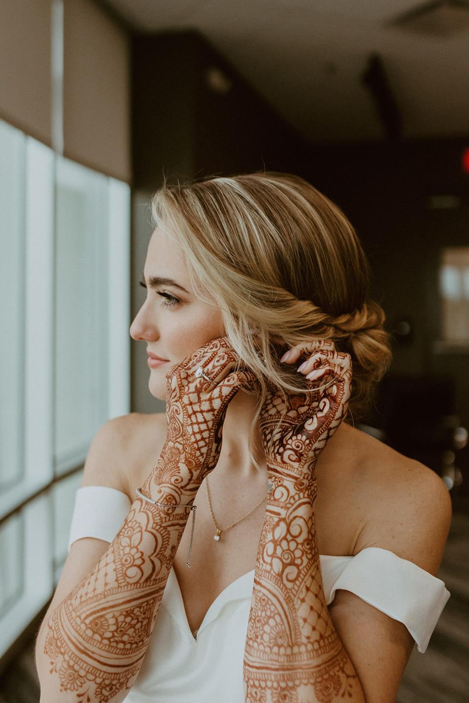 A woman with henna on her arms adjusts her earring.