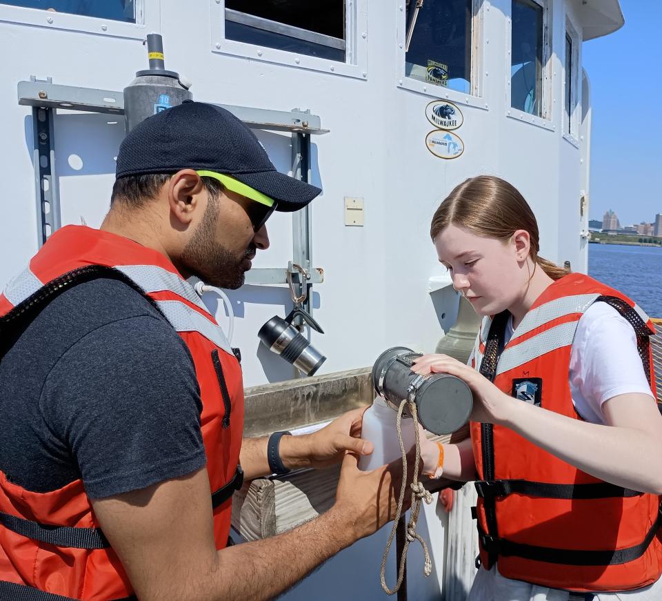 A high school student pours out greenish brown water from Lake MIchigan into a plastic container held by Samir Qureshi of UWM's School of Freshwater Sciences.