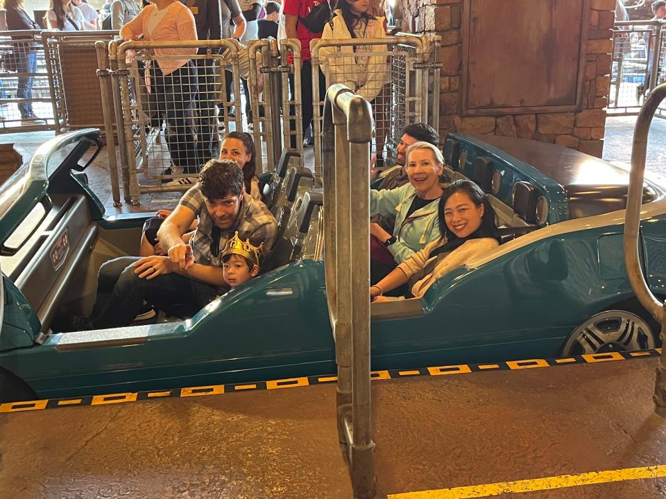 Six people smile at the camera while riding Radiator Springs Racers in Disneyland. They are seated in two rows of a teal car.