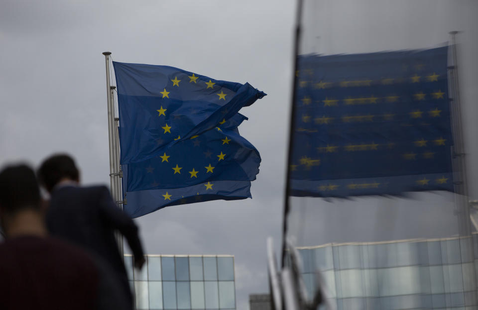 European Union flags flap in the wind as two people walk up a set of stairs outside EU headquarters in Brussels, Sunday, Oct. 13, 2019. Technical talks on Brexit continued in Brussels over the weekend with European Union Brexit negotiator Michel Barnier due to brief EU ambassadors. (AP Photo/Virginia Mayo)