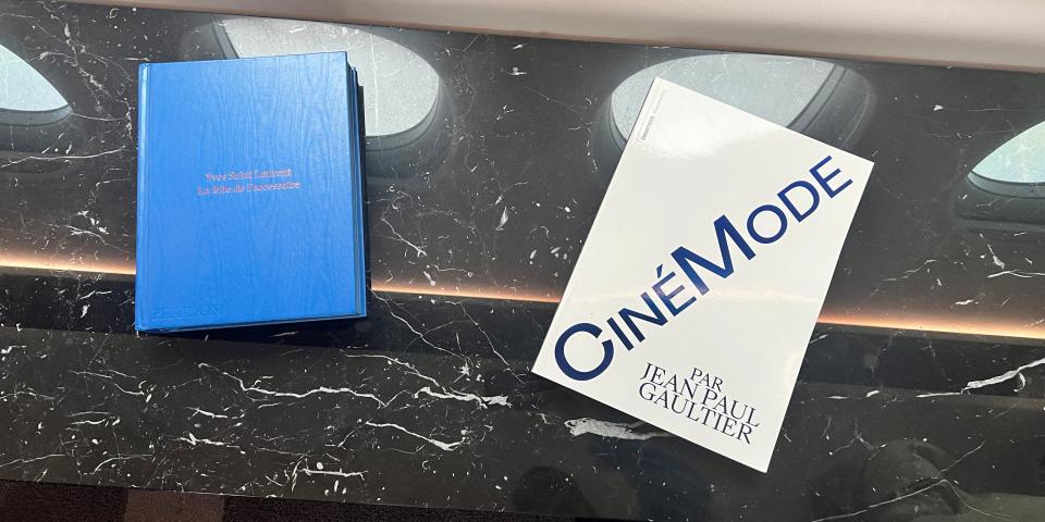 A blue book about Yves Saint Laurent and one called CineMode by Jean Paul Gaultier, atop a black marble counter