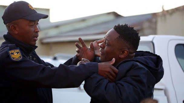 PHOTO: A family member reacts next to a police officer as forensic personnel investigate after the deaths of patrons found inside the Enyobeni Tavern, in Scenery Park, outside East London in the Eastern Cape province, South Africa, June 26, 2022. (Reuters)