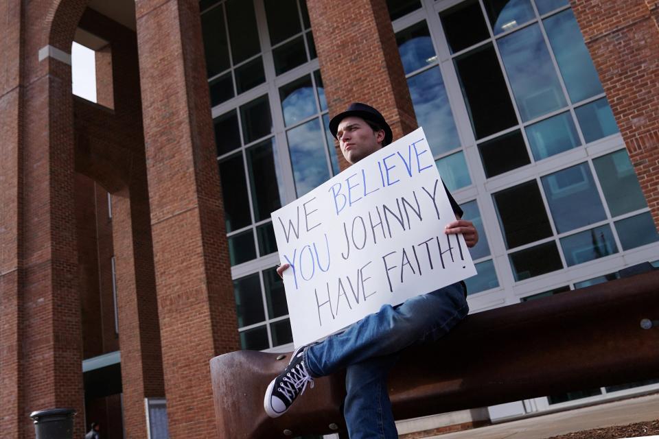 A supporter of Johnny Depp sits outside the courthouse with a placard on 12 April (REUTERS)