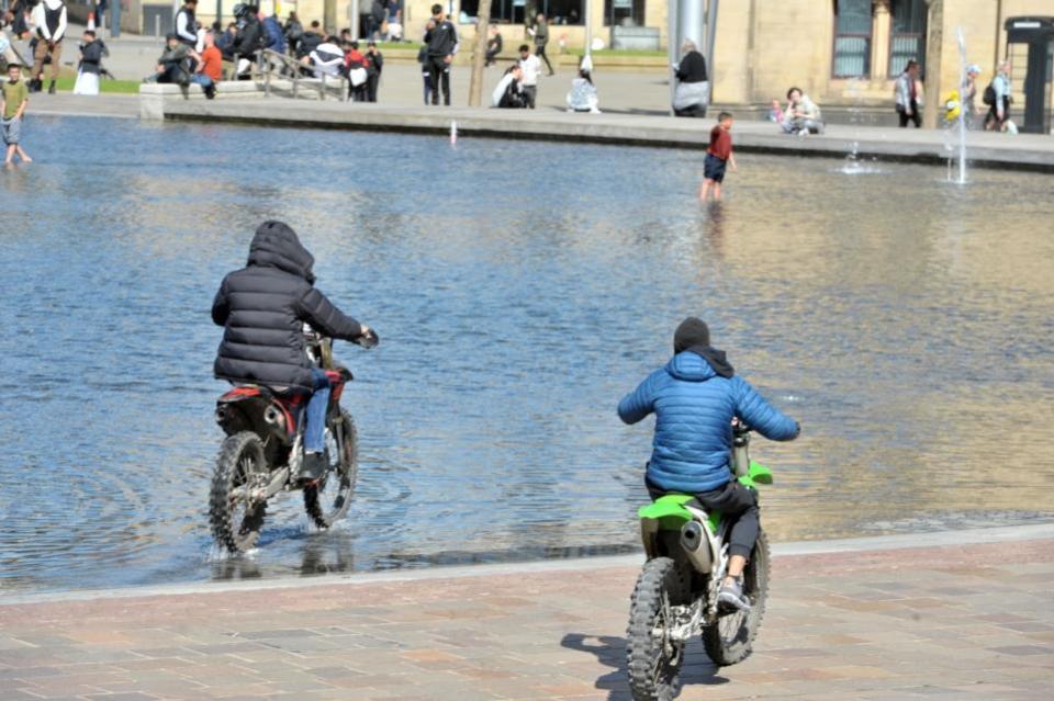 Bradford Telegraph and Argus: Two men ride through City Park in Bradford on dirt bikes as bemused children watch on