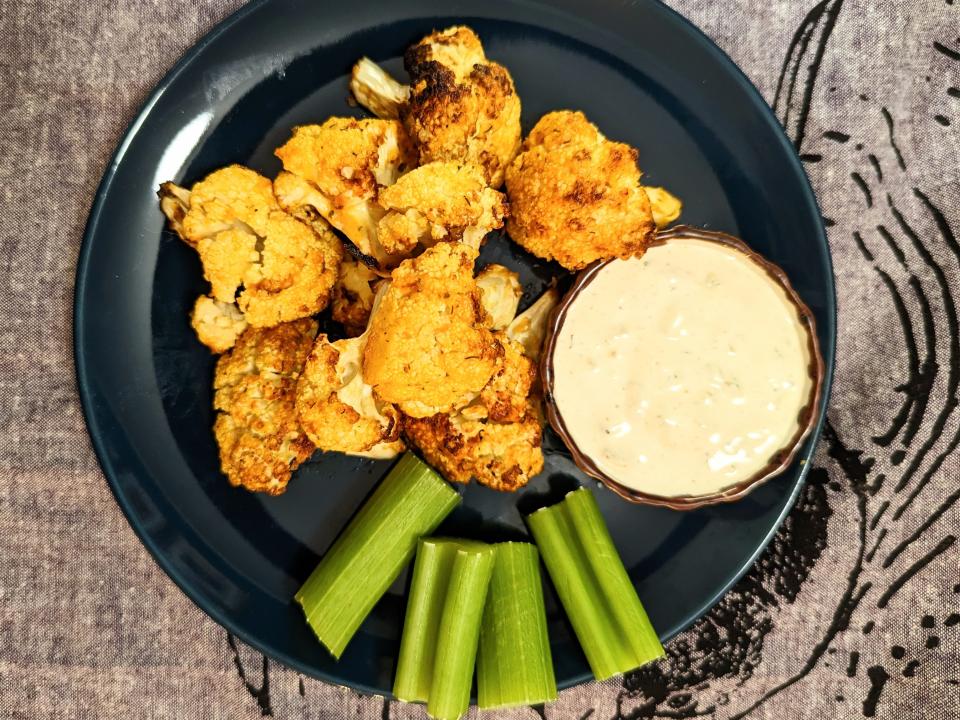 black plate with buffalo cauliflower, celrery, and a small bowl of dressing