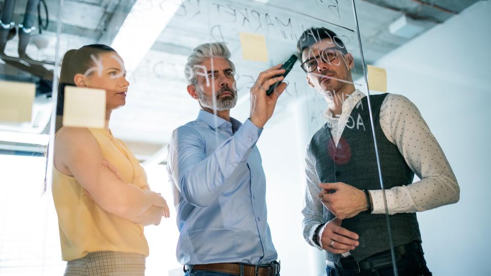 A front view of group of business people standing in an office, brainstorming.