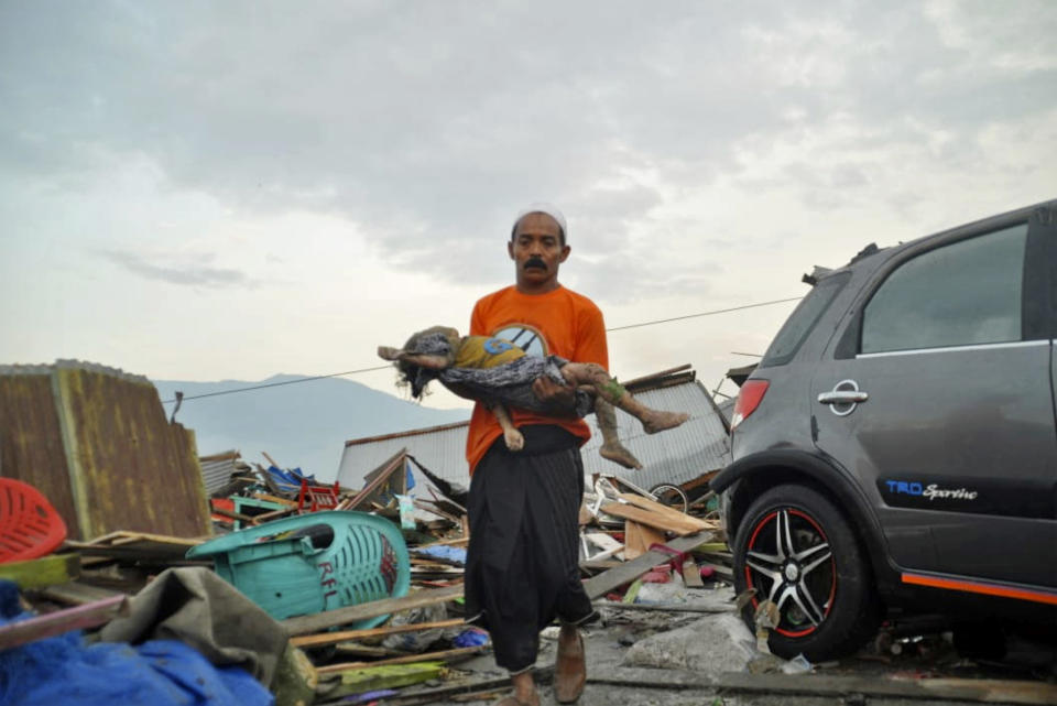 In this Saturday, Sept. 29, 2018, file photo, a man carries the body of a child who was killed in the tsunami in Palu, Central Sulawesi, Indonesia. (AP Photo/Rifki, FIle)