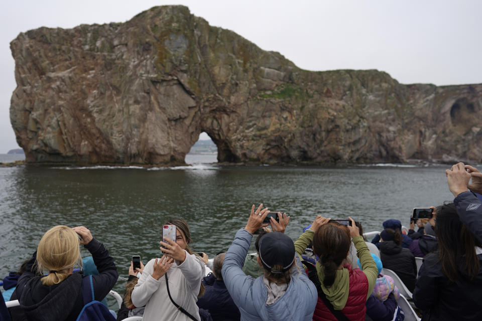 Tourists take selfies and photograph Perce Rock in Perce, Quebec, Canada, Tuesday, Sept. 13, 2022, during a Croisiere Julien Cloutier boat tour. When boats bring visitors to the island, park employees corral them to explain the trails and what they can and cannot do. (AP Photo/Carolyn Kaster)
