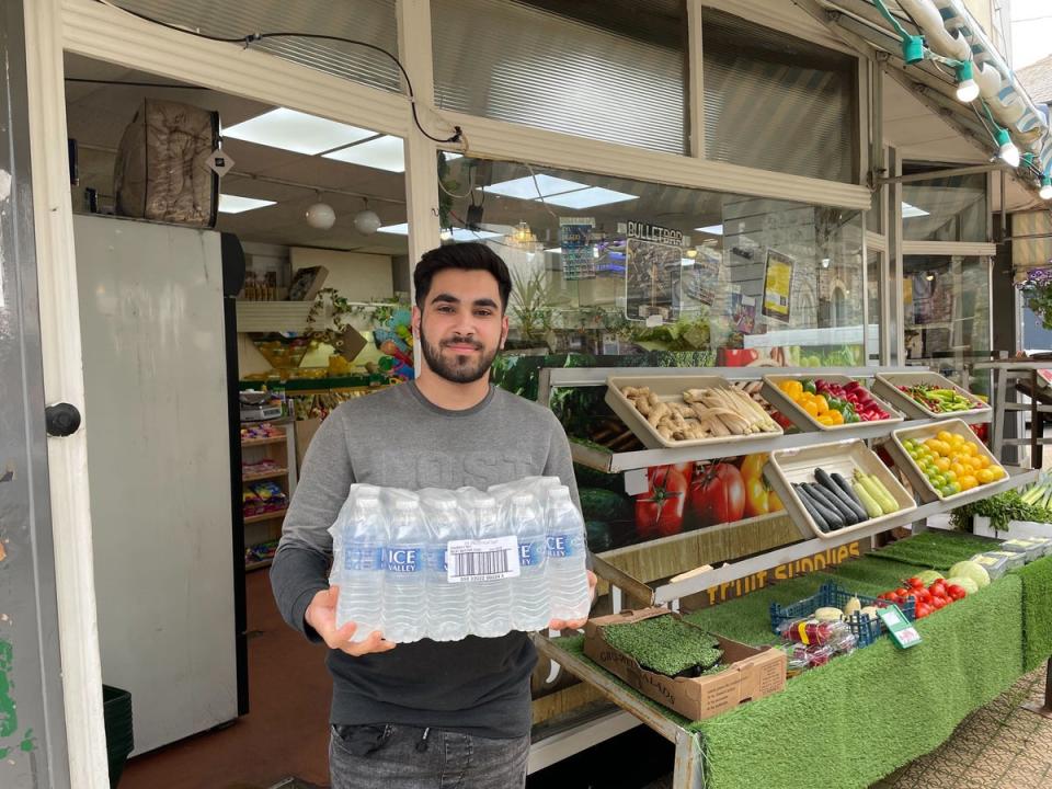 Rayan Ali, of Torbay Fruit Supplies, with the last case of water bottles his shop has been handing out to people (The Independent)