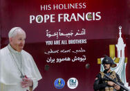 Iraqi security stand by a poster depicting Pope Francis, in Baghdad Iraq, Friday, March 5, 2021. Pope Francis heads to Iraq on Friday to urge the country's dwindling number of Christians to stay put and help rebuild the country after years of war and persecution, brushing aside the coronavirus pandemic and security concerns. (AP Photo/Andrew Medichini)