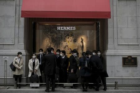 Business people shelter from the rain under outside a luxury store in Tokyo, Japan, February 15, 2016. REUTERS/Thomas Peter