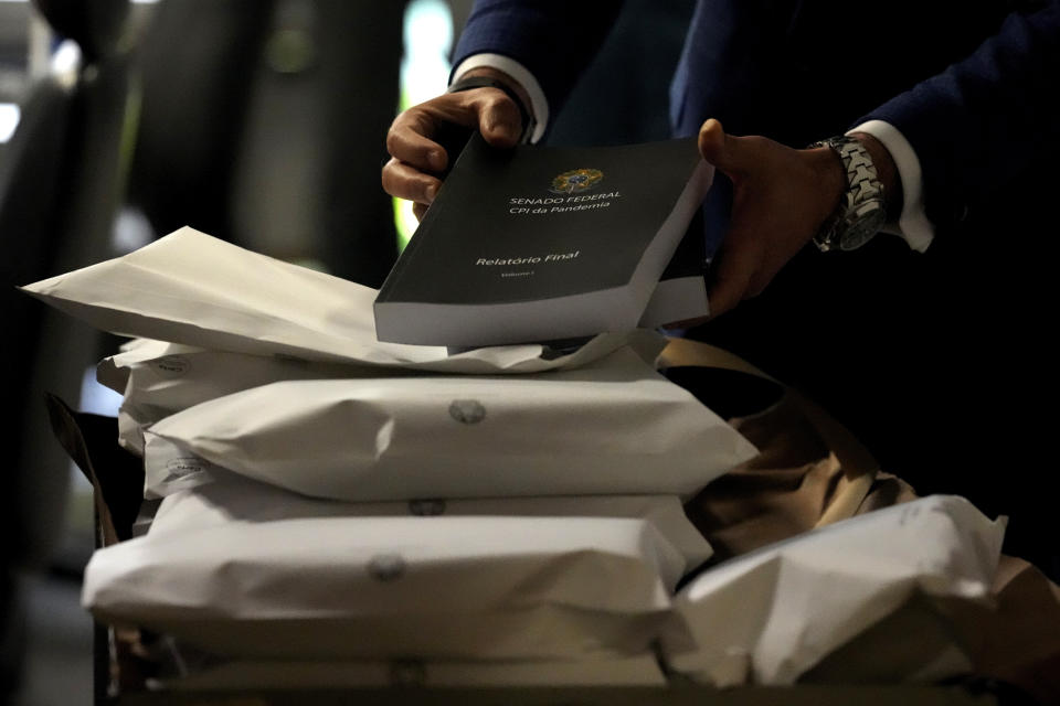 A Senate employee removes a copy of a Senate commission report on the government's handling of the COVID-19 pandemic at the Federal Senate in Brasilia, Brazil, Wednesday, Oct. 20, 2021. A senator formally presented the report recommending President Jair Bolsonaro be indicted on criminal charges for allegedly bungling Brazil’s response to the pandemic and pushing the country’s death toll to second-highest in the world. (AP Photo/Eraldo Peres)