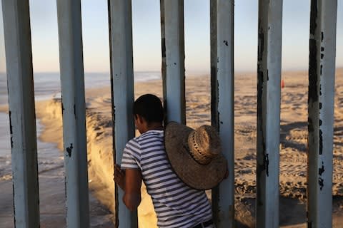 A man looks through the US-Mexico border fence into the United States on September 25, 2016 in Tijuana, Mexico  - Credit: John Moore/Getty Images