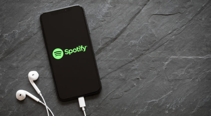 Spotify (SPOT) logo is on the screen of a smartphone with headphones plugged in.