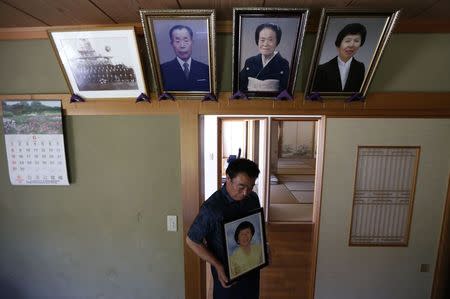 Mikio Watanabe holds a portrait of his late wife Hamako under photographs of his ancestors and Hamako (top R) at his home at Yamakiya district in Kawamata town, Fukushima prefecture June 23, 2014.REUTERS/Issei Kato