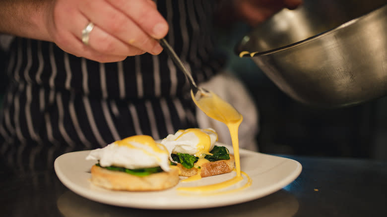 Chef drizzling hollandaise sauce on eggs Benedict