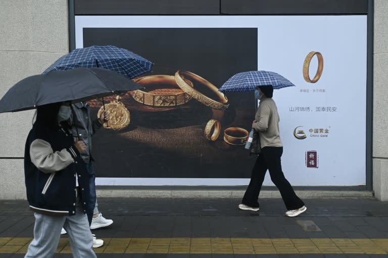 Des passants avec des parapluies marchent devant un panneau publicitaire à Pékin le 10 avril 2024 (WANG Zhao)