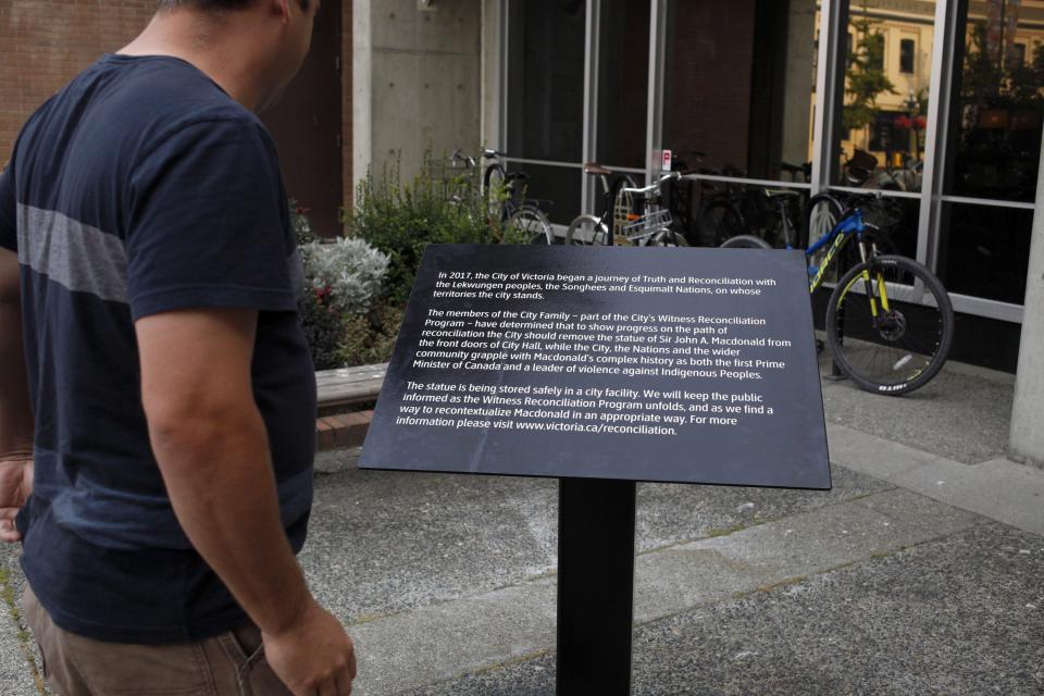 A second plaque has been installed to replace a bronze statue of Canada’s first Prime Minister Sir John A. Macdonald after it was vandalized shortly after the removal of the statue over the weekend. People walk by the plaque daily as it stands in front of City Hall Victoria, B.C., on Tuesday, Aug. 14, 2018. (Photo by Chad Hipolito, The Canadian Press)