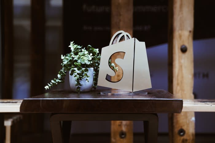 A window with the Shopify logo prominently displayed next to a potted plant.