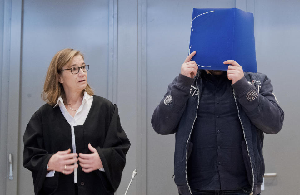 The defandant covers his face with a folder as he and his lawyer Ulrike Baumann, left, arrive at the temporay Oldenburg district court at the Weser Ems halls in Oldenburg, Germany, Tuesday, Oct. 30, 2018. The nurse serving a life sentence for two murders is going on trial on charges that he killed a further 100 patients at two hospitals in Germany. (Julian Stratenschulte/dpa via AP, Pool)
