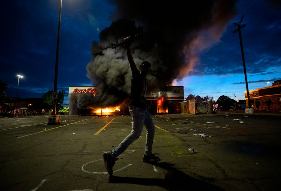 A man poses in the parking lot of an AutoZone store in flames May 27.