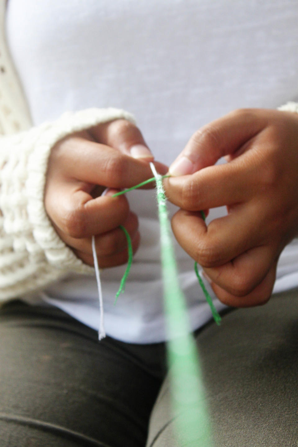 A girl makes a friendship bracelet sitting down.