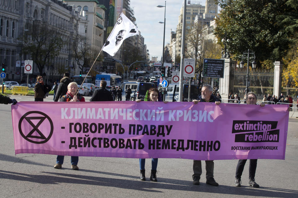 Activists hold a banner written in the Russian language during a protest performance at the Cibeles fountain in central in Madrid, Spain, Tuesday, Dec. 3, 2019. Some 20 activists from the international group called Extinction Rebellion cut off traffic in central Madrid and staged a brief theatrical performance to protest the climate crisis. The activists held up a banner in Russian that read "Climate Crisis. To speak the truth. To take action immediately." (AP Photo/Paul White)