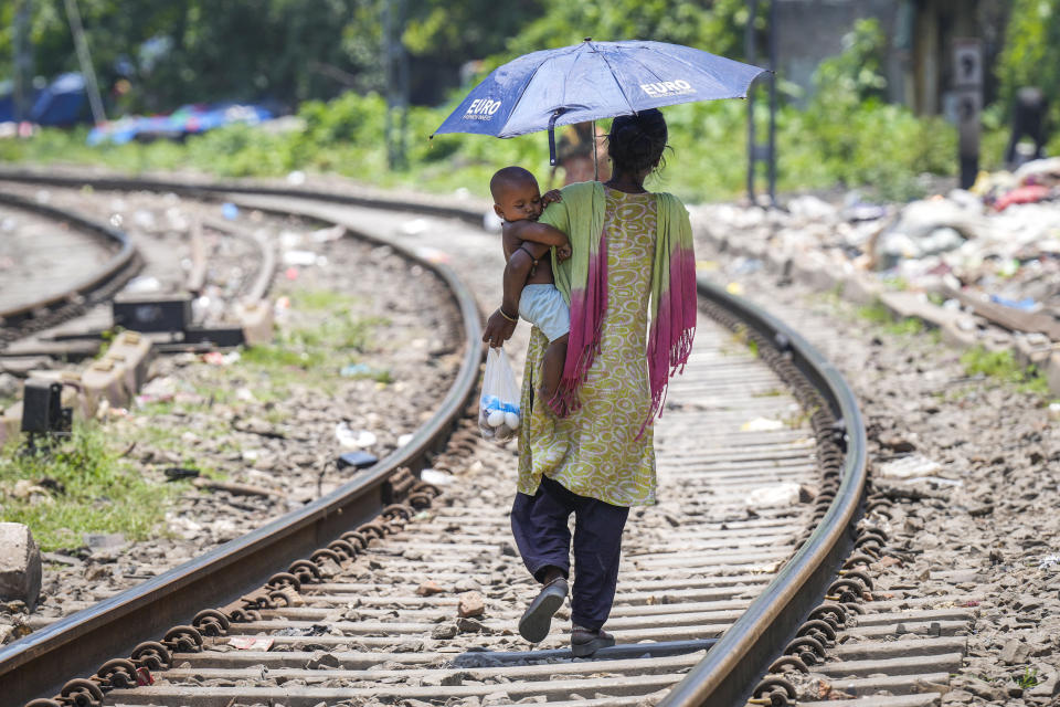 Una mujer se protege con un paraguas mientras camina por una vía de tren con un bebé en brazos en un día de mucho calor, en Guwahati, India, el 25 de mayo de 2024. (AP Foto/Anupam Nath)